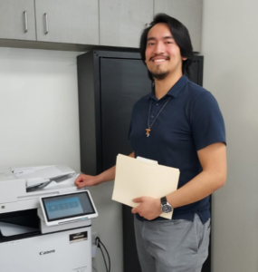 Tristen holding a folder near a printer at the Men's Shelter